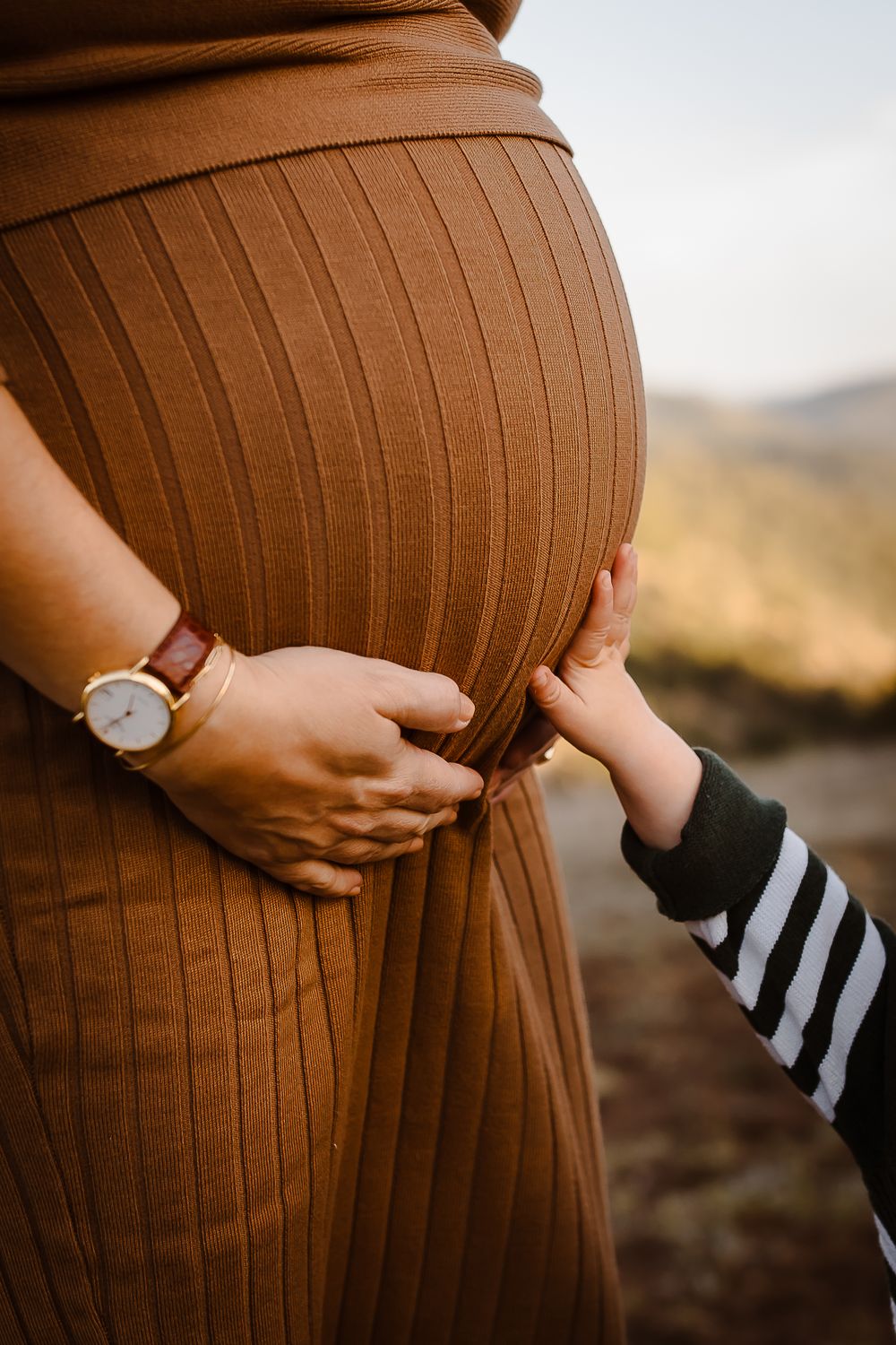 A child gently touches their mother's baby bump in the Denver foothills