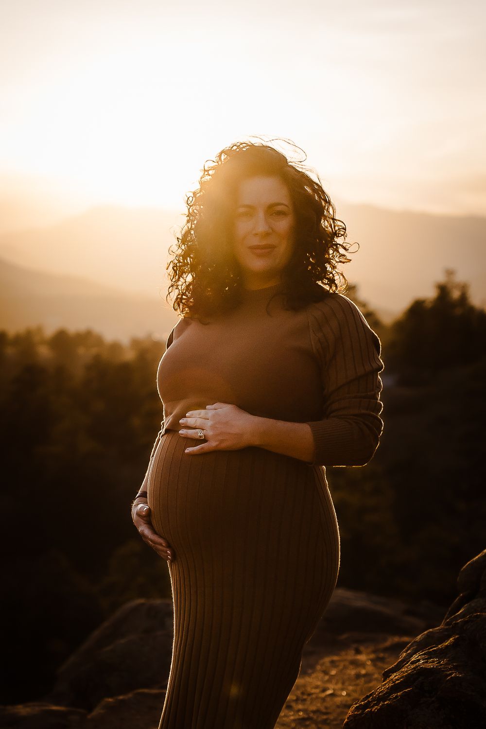 Mother gently cradles her baby bump at golden hour in the Denver foothills