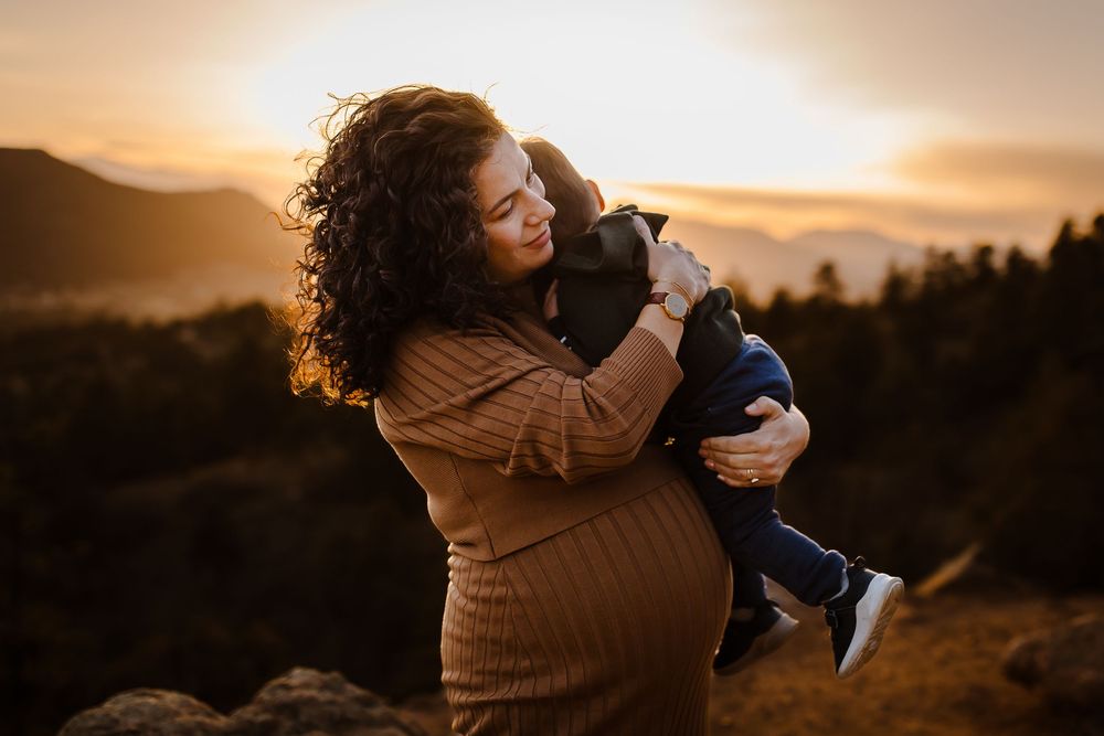 Pregnant mother holds her young child at golden hour with mountain background