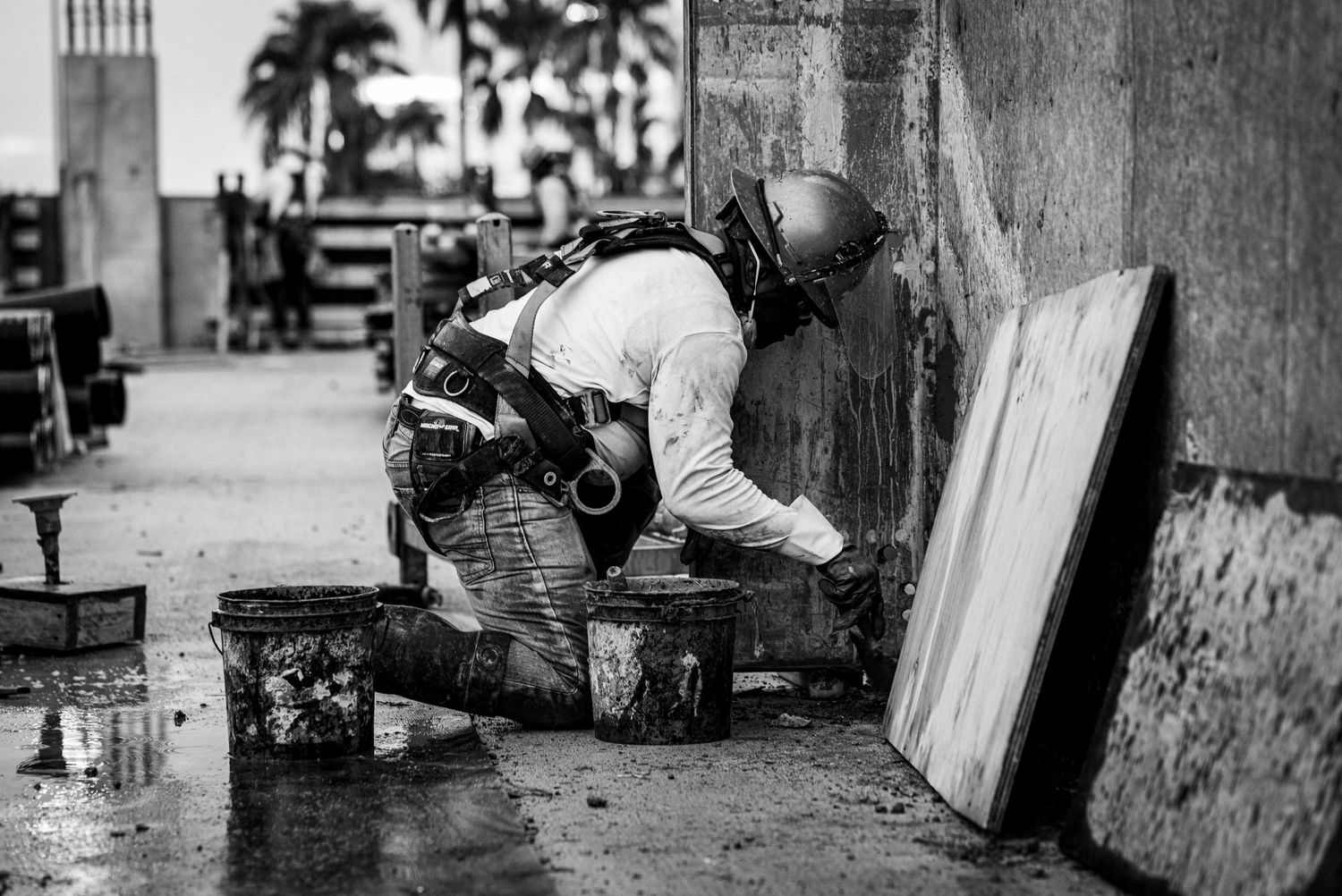 Law enforcement officer in tactical gear crouches behind a wall during a field operation in black and white photography.