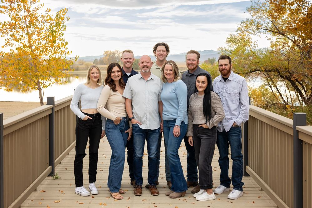 Group portrait of nine people standing together on wooden bridge in autumn setting.