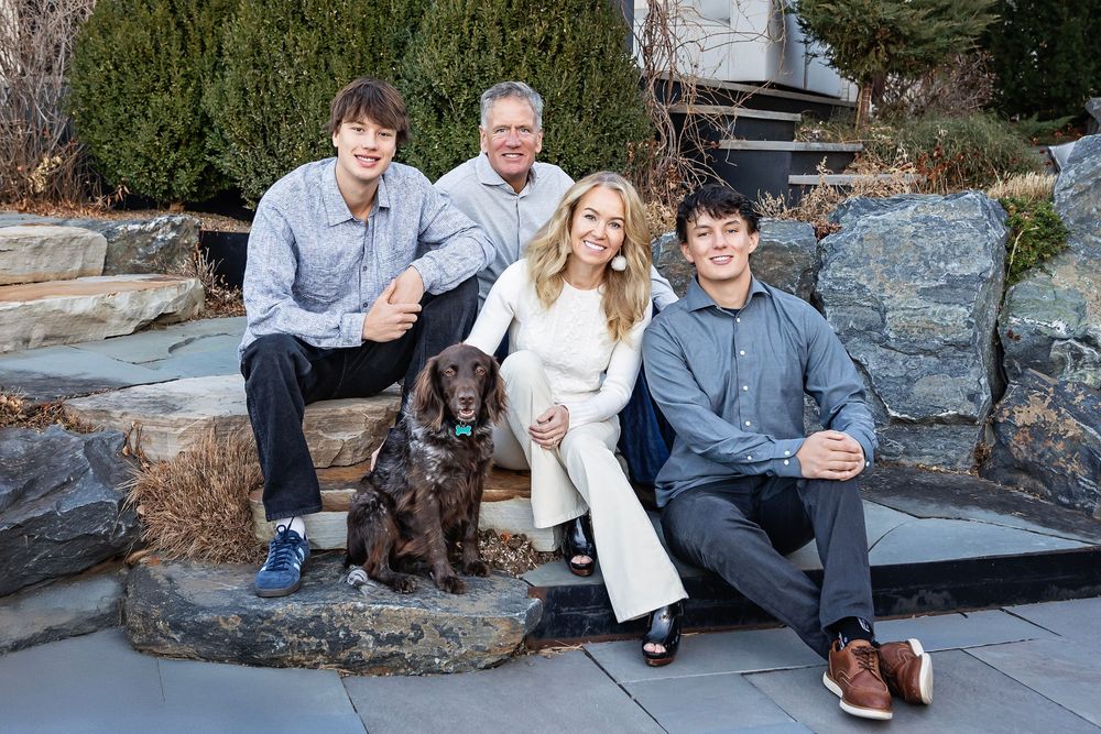 Family with chocolate lab dog poses outdoors on stone steps during photo session.