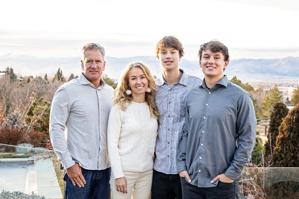 Family of four poses together with mountain vista and lake in background.