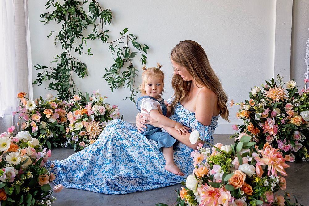 Mother and baby in matching blue floral dresses against floral backdrop.
