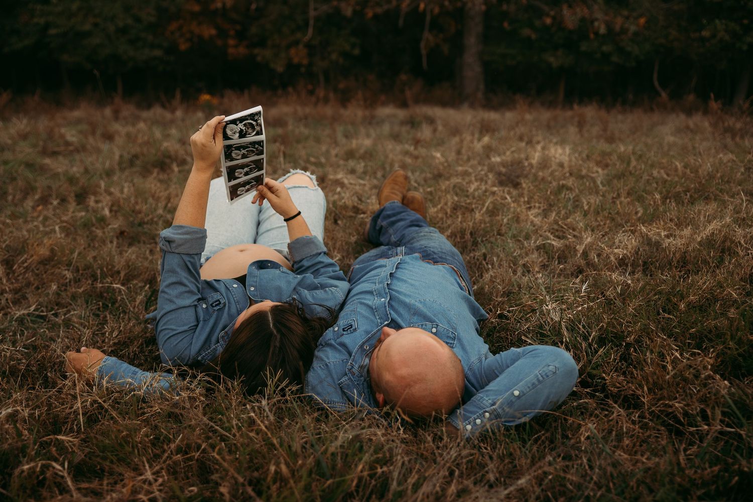 Creative family photo shoot with members lying in grass at sunset.