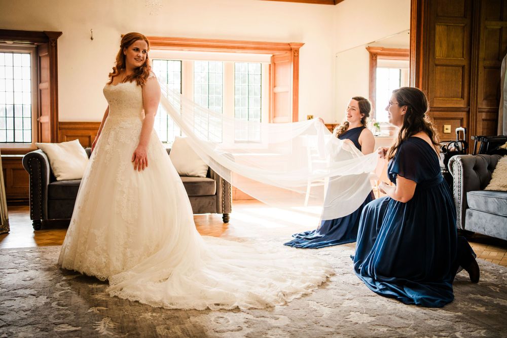bridesmaids helping a bride to get ready at Dalston hall, cumbria and lifting her long veil