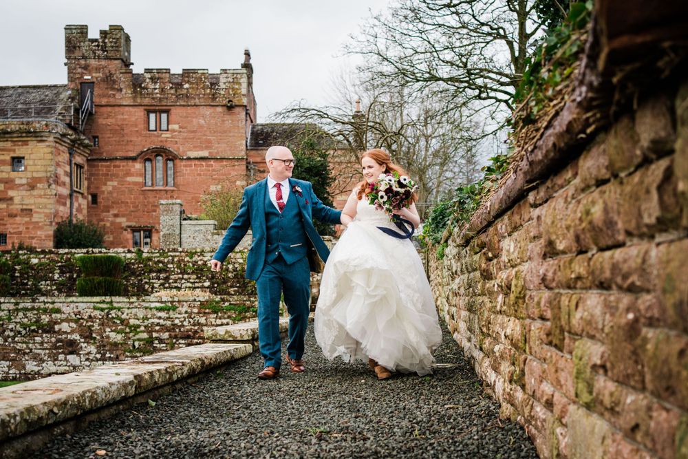 Bride and groom walking along a path with Dalston Hall in the background