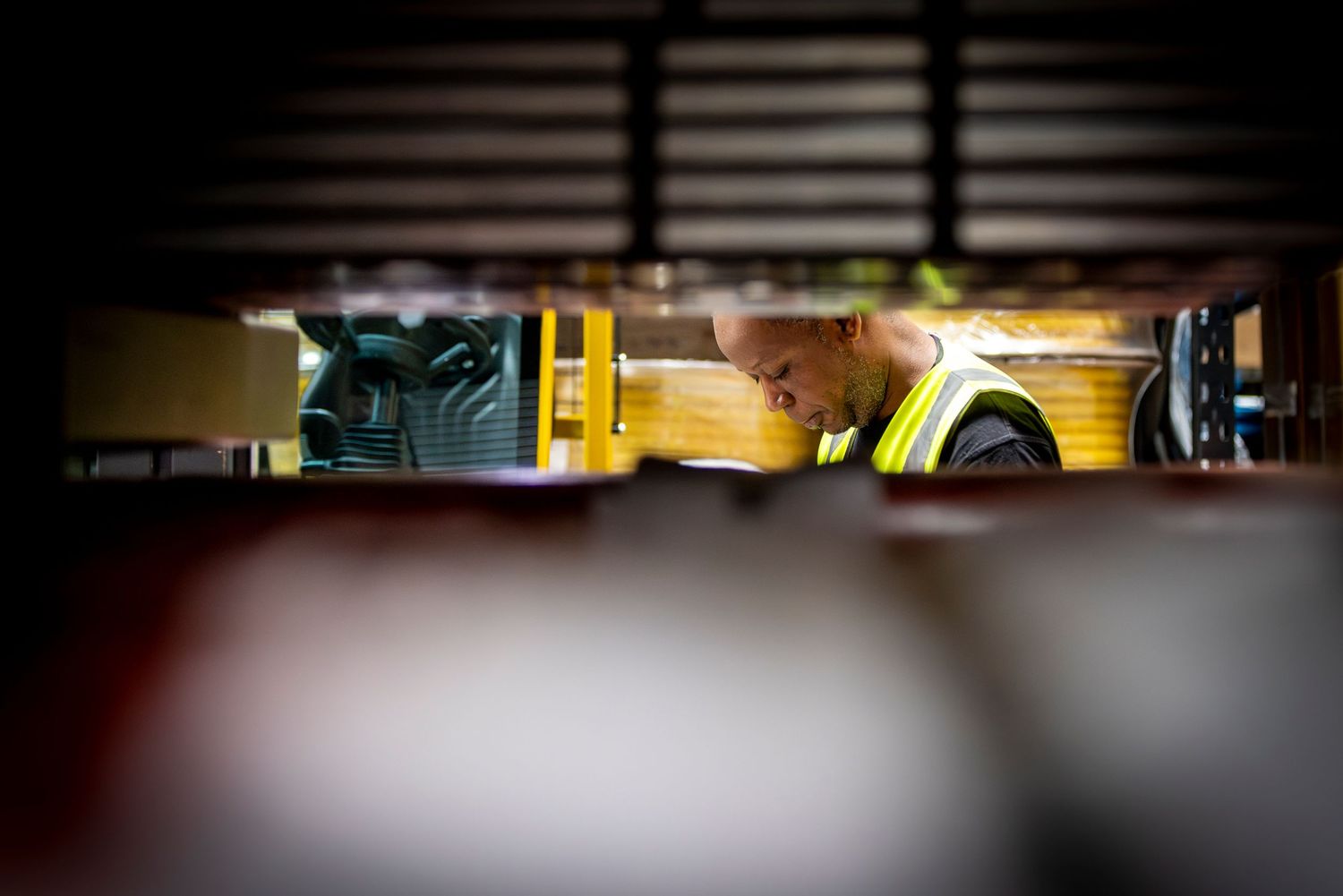 Glimpse of yellow industrial equipment through storage shelf slats.