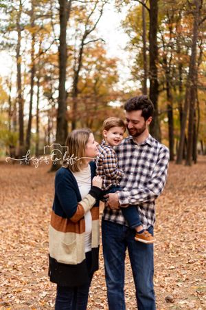 Family portrait in a wooded setting with fallen autumn leaves.