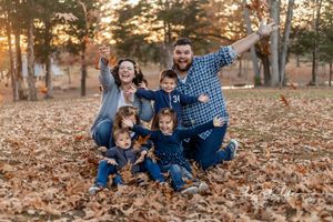Joyful family photo with multiple children playing in fallen autumn leaves.