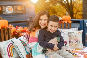 Smiling siblings sitting in truck bed with autumn decorations and pumpkins.