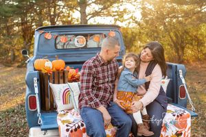 Family sitting in vintage blue pickup truck bed with fall decorations and pumpkins.