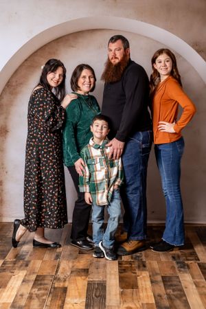 Family group portrait standing under arch against textured wall and wooden floor.