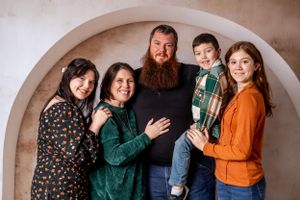 Casual family portrait with rustic arch backdrop and wooden flooring.