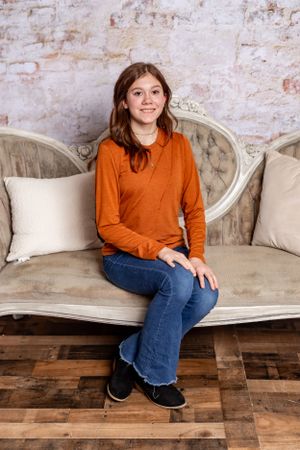 Person in orange sweater sitting on vintage sofa against textured wall.