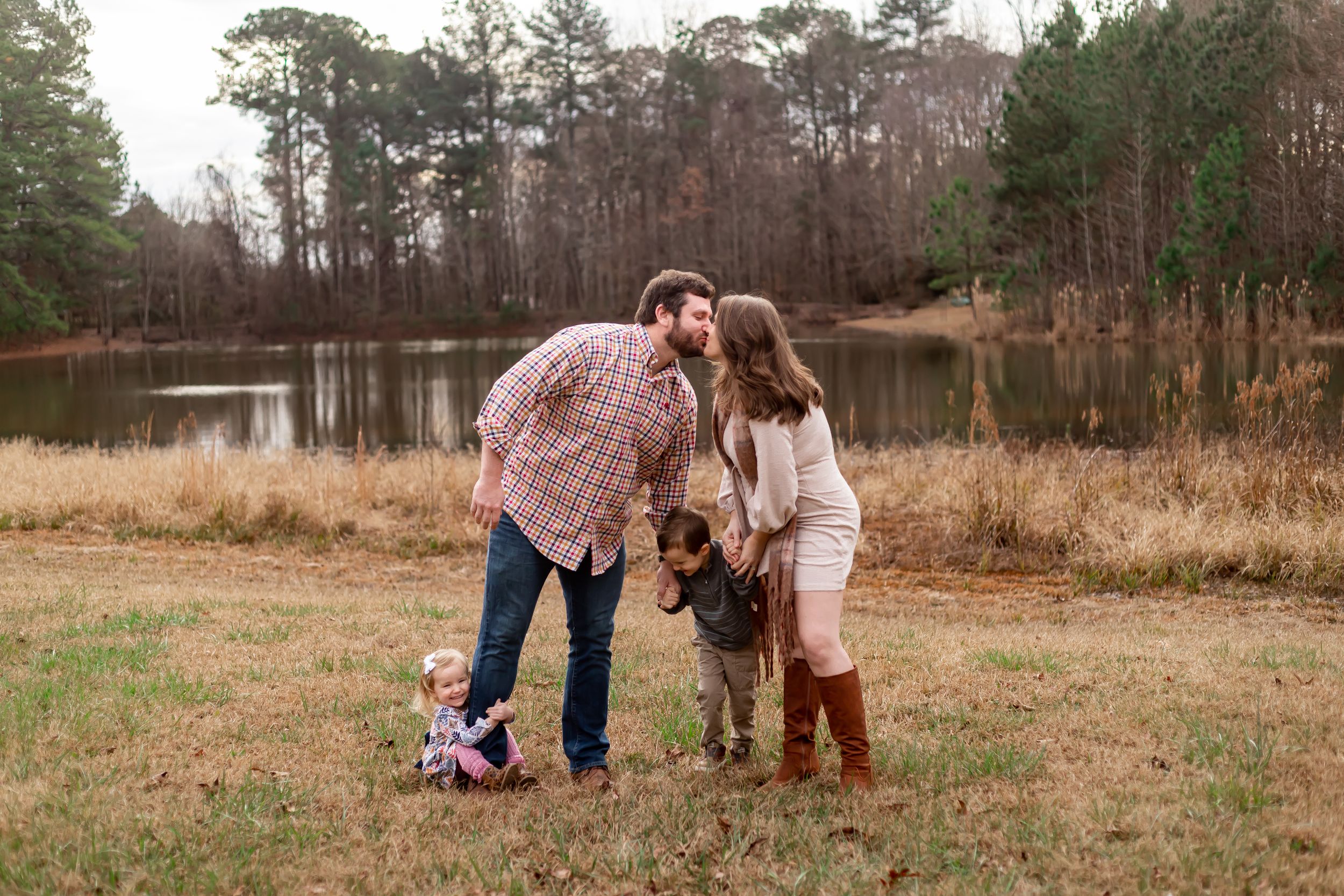Family portrait by a pond in autumn with rustic countryside backdrop.