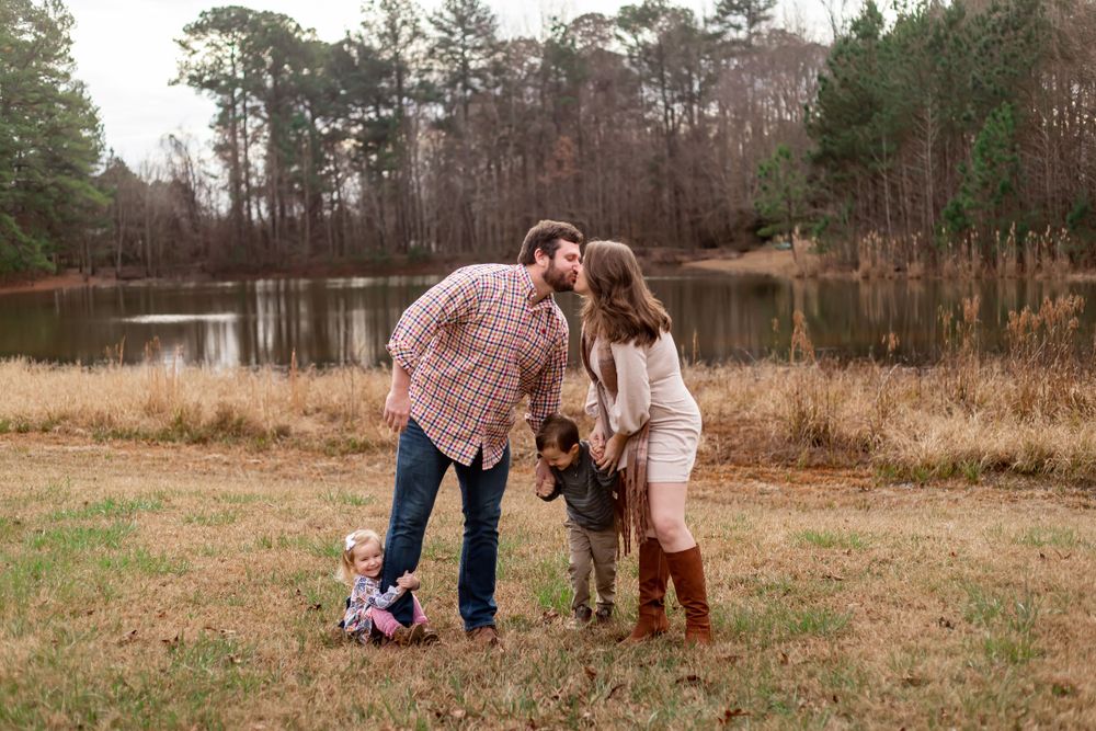 Family portrait by a pond in autumn with rustic countryside backdrop.