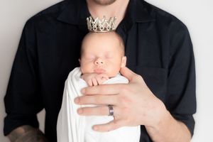 Father holding swaddled newborn baby wearing a small crown, captured in a tender newborn photography portrait.