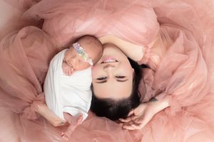 Mother and newborn baby girl in pink tulle dress lying together in a beautiful studio portrait photo.