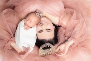 Mother and newborn baby lying on pink tulle fabric, mom wearing crown and jeweled necklace.