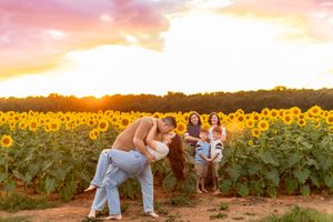 Couple dancing in a sunflower field at sunset with family watching in the background.