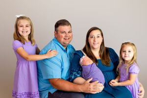 Family portrait with parents and children wearing coordinating purple and blue outfits.