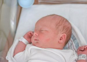 Peaceful newborn baby sleeping in white clothing against a light background.