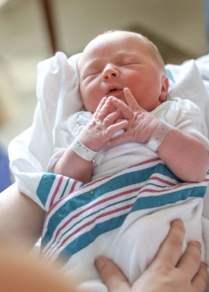 Newborn baby wearing hospital bracelet wrapped in white and striped blanket.