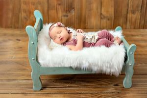 Sleeping newborn on turquoise vintage-style doll bed with white fur mattress.