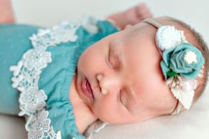 Peaceful sleeping infant in teal lace dress with matching floral headband.