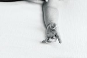 Black and white close-up photograph of tiny newborn hand against white background.