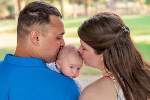 Parents share tender moment with newborn baby outdoors during family photo session.