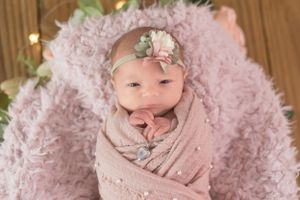 Newborn wrapped in pink swaddle on fluffy pink blanket with twinkling lights in background.