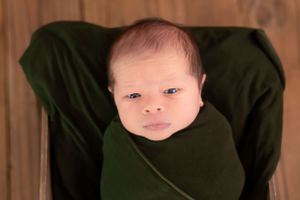 Alert newborn wrapped in dark green swaddle against wooden background.