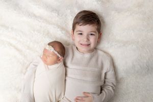 Two siblings in matching cream sweaters posing together on white textured backdrop.