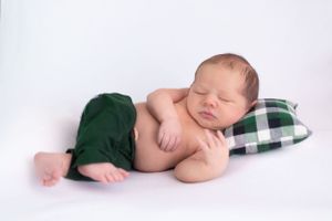 Sleeping newborn resting on plaid pillow with green shorts in studio setting.