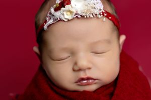 Sleeping baby wearing delicate floral headband against deep red background.