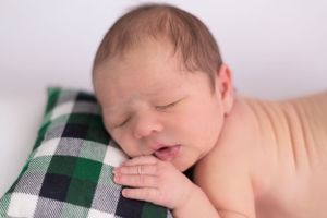 Sleeping newborn resting on green plaid pillow in natural posed portrait.