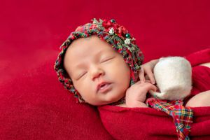 Sleeping newborn wearing festive holiday bonnet on red background.
