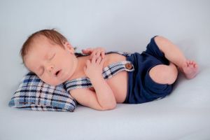 Sleeping newborn in blue outfit lying on plaid pillow during photoshoot.