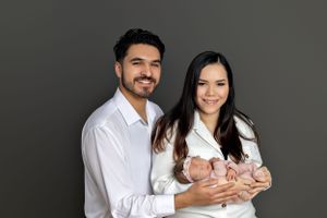 Couple in white shirts holding newborn against grey background.