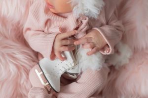 Close-up of tiny white ice skates held against pink knit clothing on furry blanket.