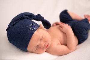 Sleeping newborn wearing navy blue hat and pants on white background.