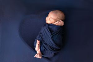 Sleeping newborn wrapped in navy blue blanket on dark background.