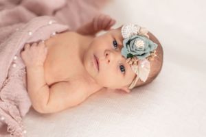 Newborn in pink wrap with delicate blue floral headband on white background.