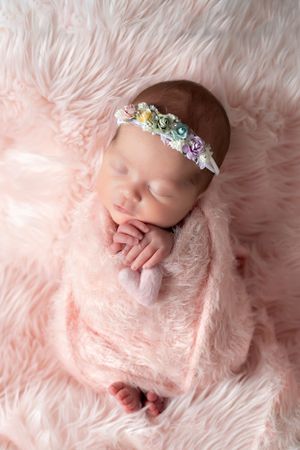 Sleeping newborn with floral headband on pink furry background.