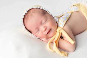 Sleeping newborn in yellow and white outfit with lace trim on white background.