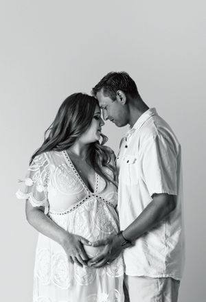 Black and white intimate maternity portrait of a couple in white clothing.