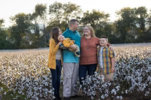 Family group poses together in blooming cotton field during sunset.