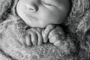 Close-up black and white portrait of sleeping newborn wrapped in soft knit blanket.
